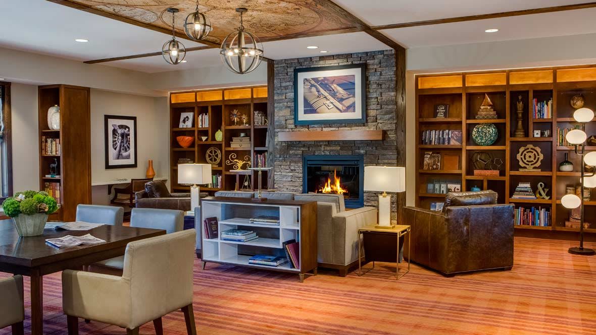 A cozy living room with a fireplace, surrounded by bookshelves and comfortable seating.