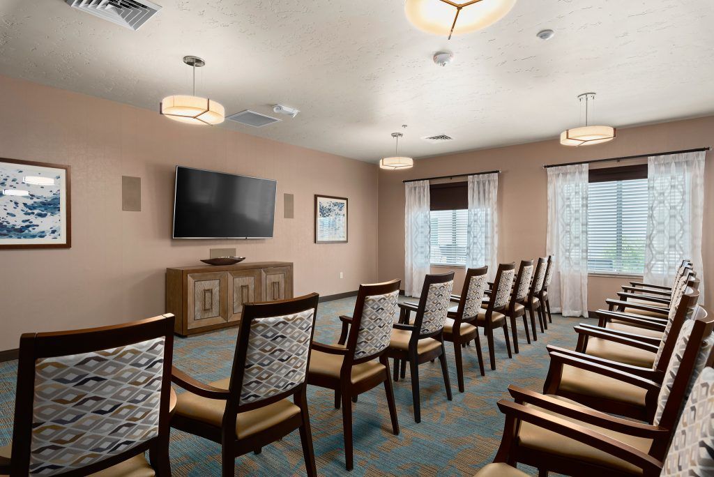 A well-arranged conference room with rows of chairs facing a mounted TV screen, featuring modern lighting and decor.