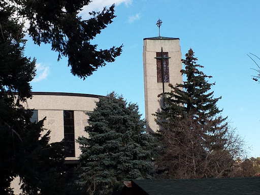 A church building featuring a prominent tower and surrounded by trees under a blue sky.