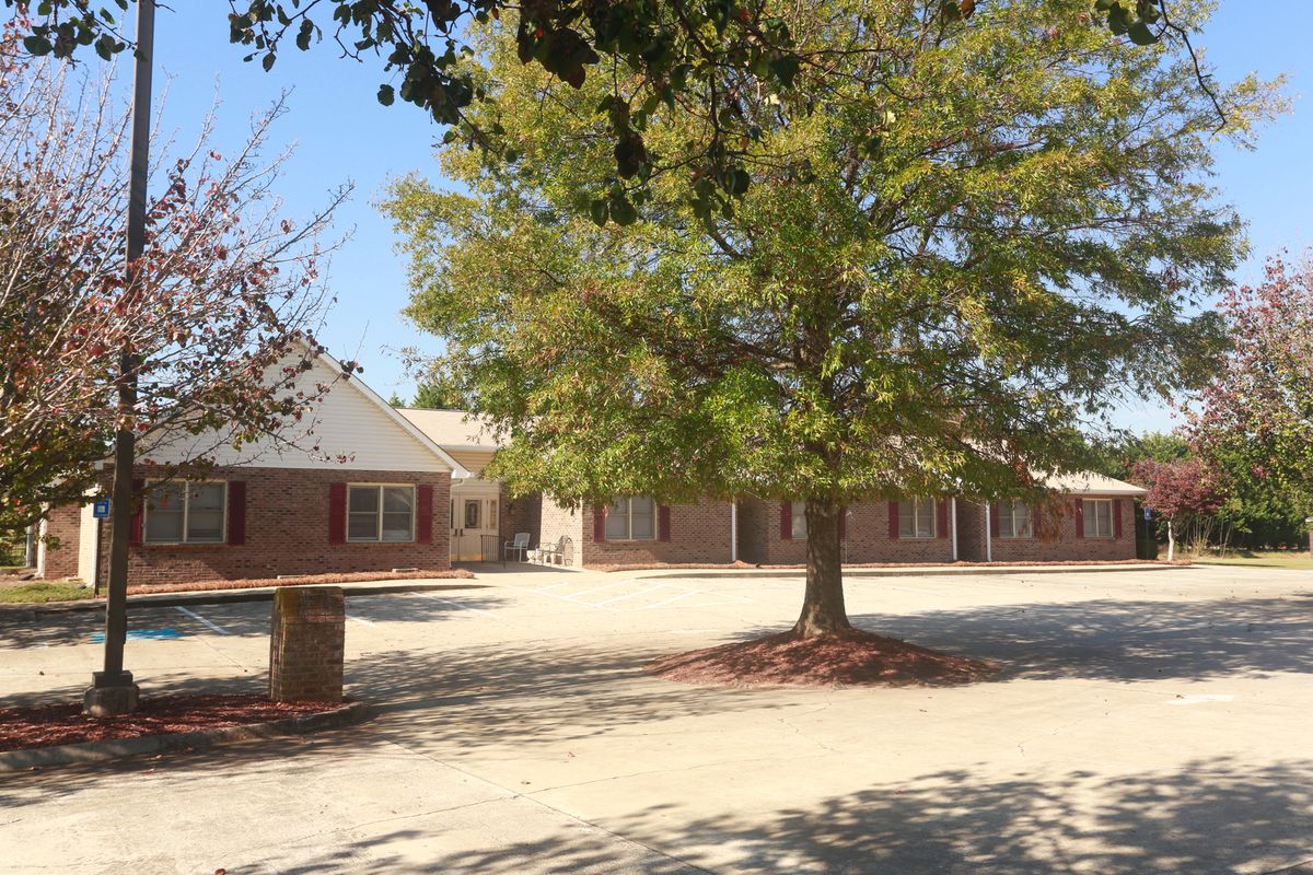 A sunny outdoor view of a brick building and a large tree.