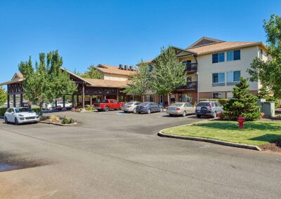 A hotel with a parking lot in front, surrounded by trees under a clear blue sky.