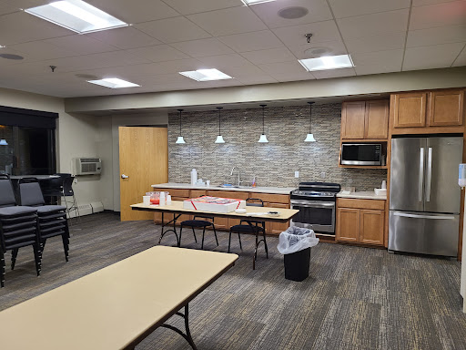 A modern breakroom featuring a kitchen area with wooden cabinets, appliances, and seating arrangements.