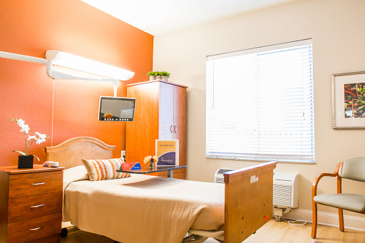 A cozy hospital room featuring a bed, modern furnishings, and natural light from a large window.