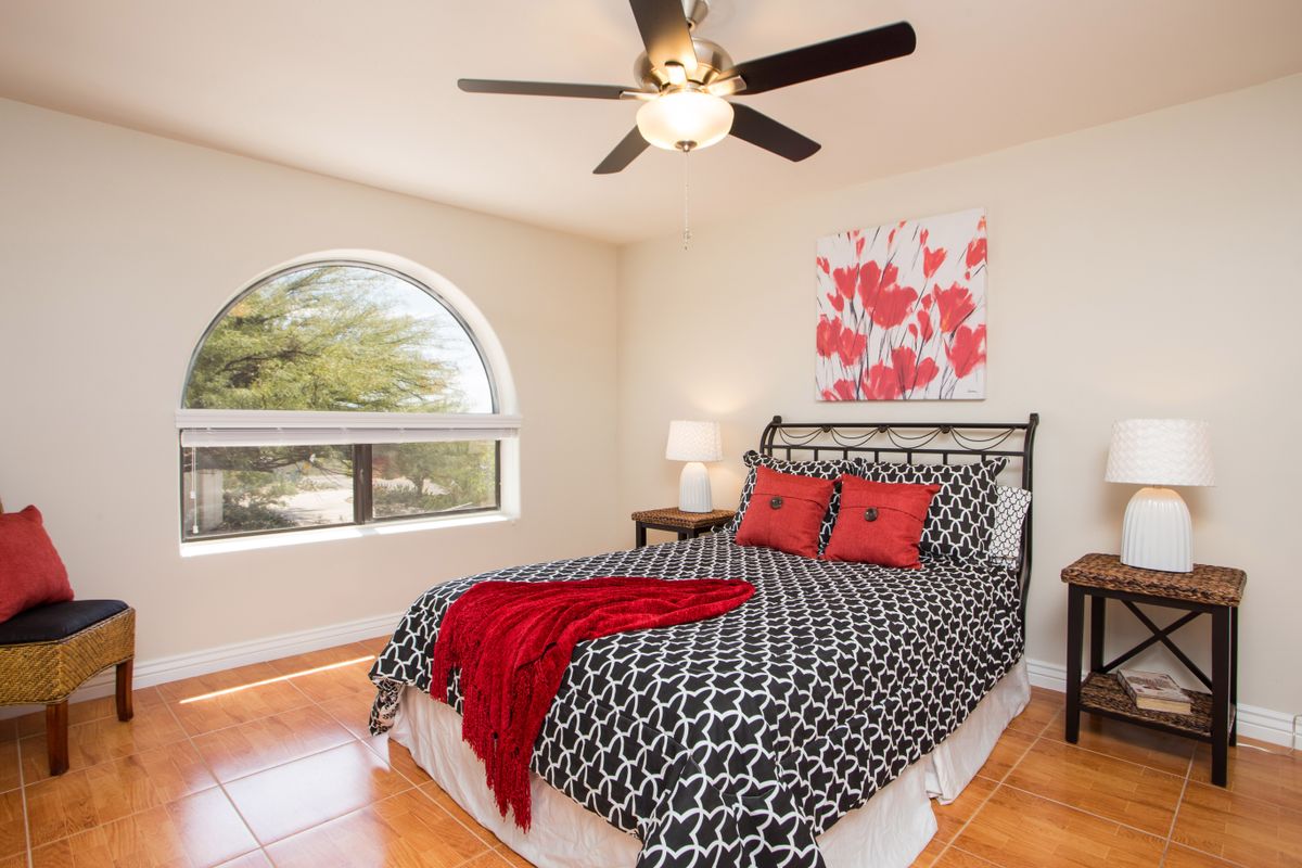 A cozy bedroom with a geometric patterned bedspread, red accents, and a large arched window.