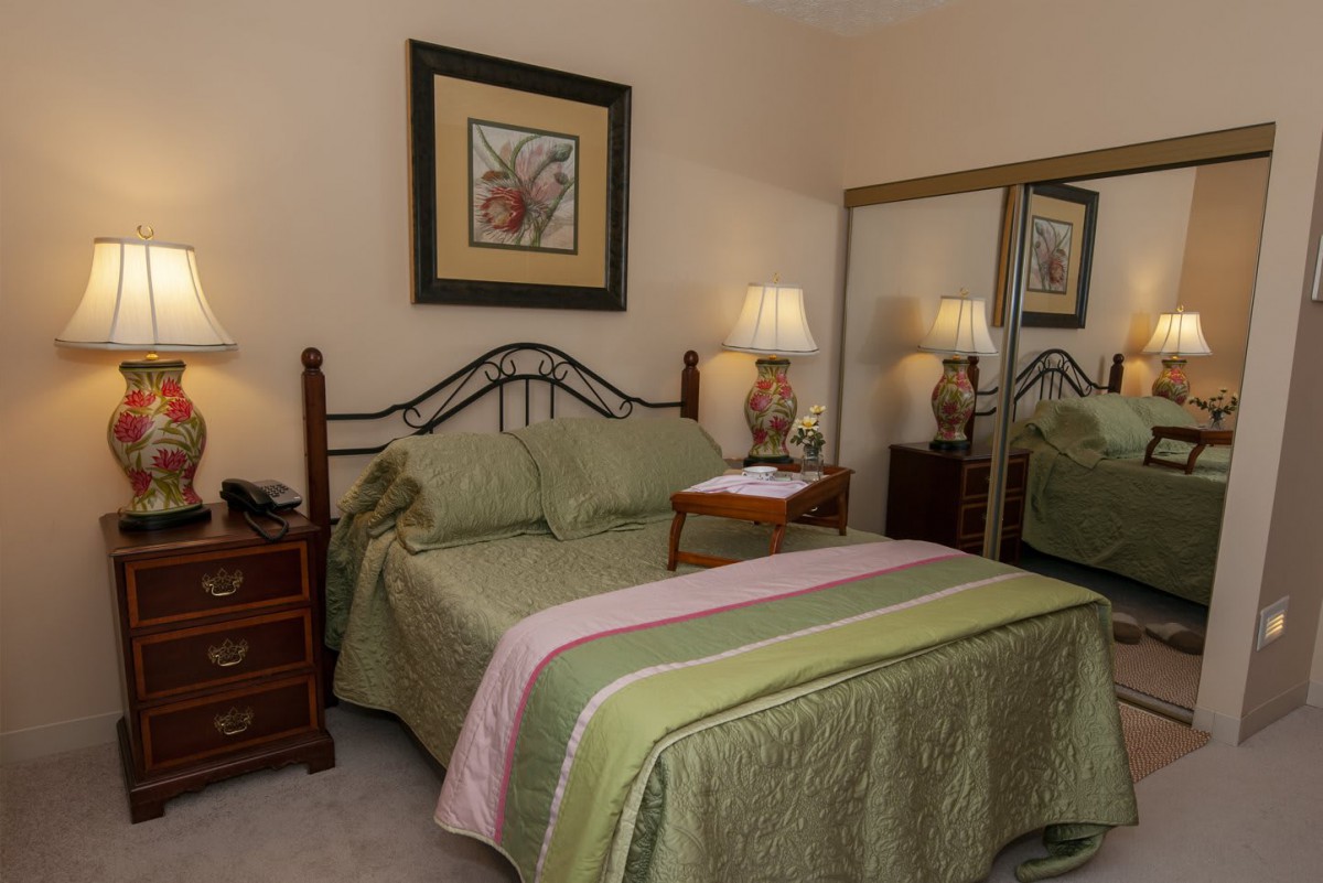 A cozy bedroom with a neatly made bed, nightstands, lamps, and mirrored closet doors.