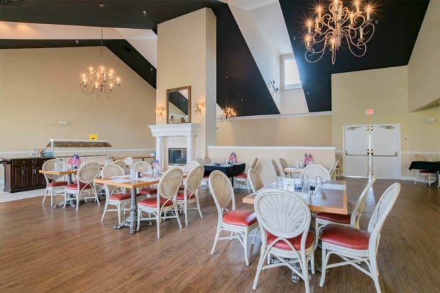 An elegant restaurant dining area featuring chandeliers, a fireplace, and neatly arranged tables and chairs.