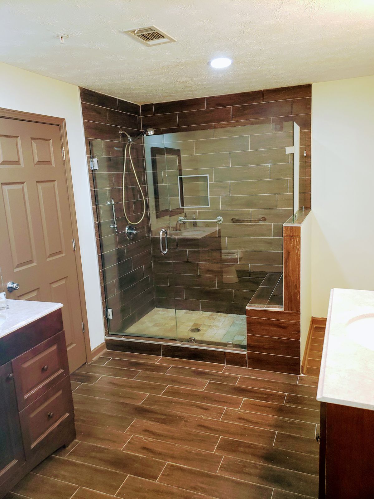 A modern bathroom featuring a glass-enclosed shower with wood-like tile flooring and walls.