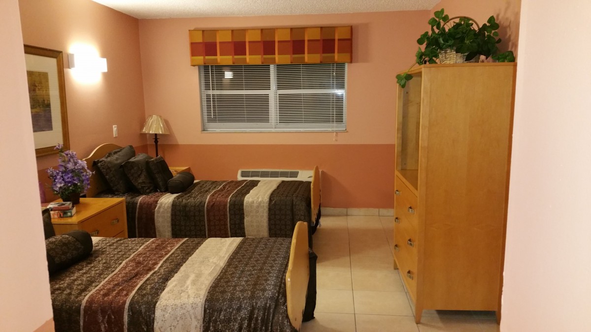 A cozy bedroom with twin beds featuring striped bedding, a window with curtains, and a dresser topped with a plant.