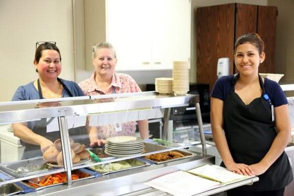 Cafeteria staff members standing behind a lunch counter ready to serve.