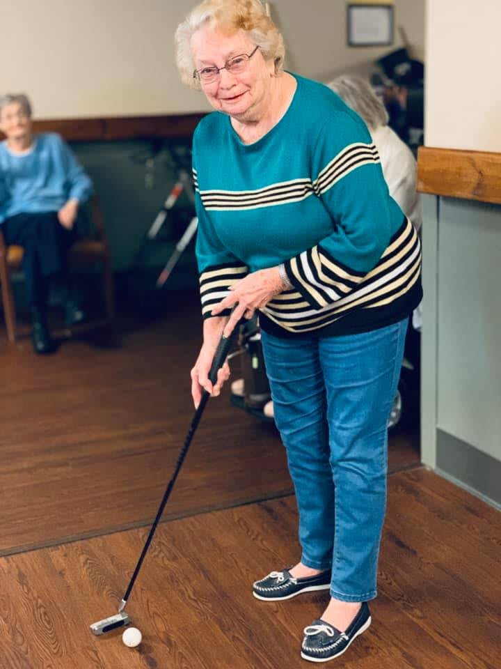 An elderly woman practicing her golf swing indoors.