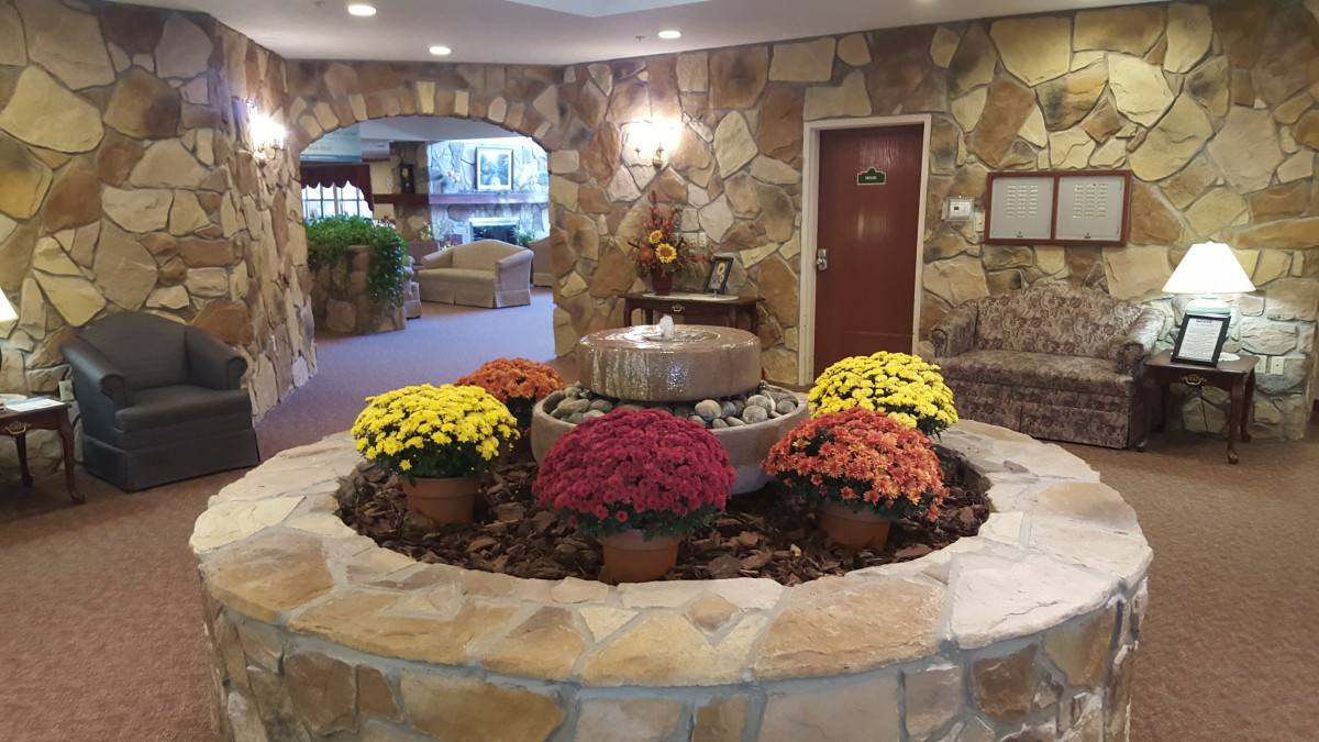 A cozy lobby with a central fountain surrounded by colorful flowers and stone walls.