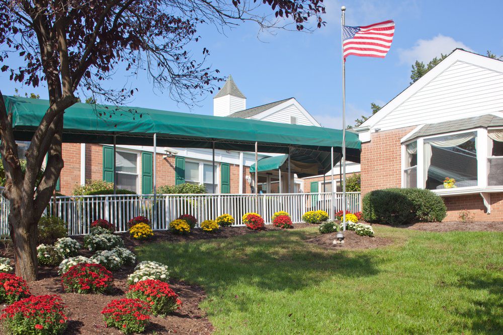 A building with a green awning and landscaped garden featuring colorful flowers and an American flag.