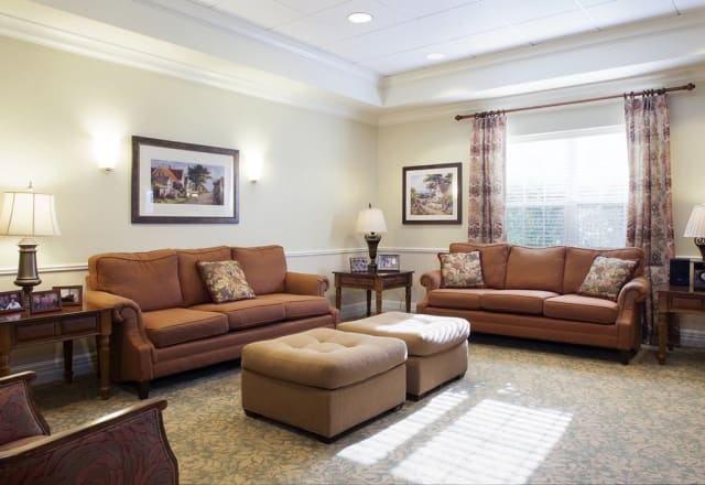 A cozy living room with two brown sofas, matching ottomans, and decorative artwork on the walls.