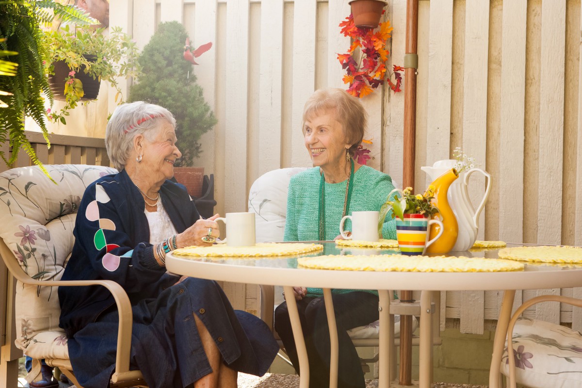 Two elderly women enjoying a conversation over tea on a sunny patio.