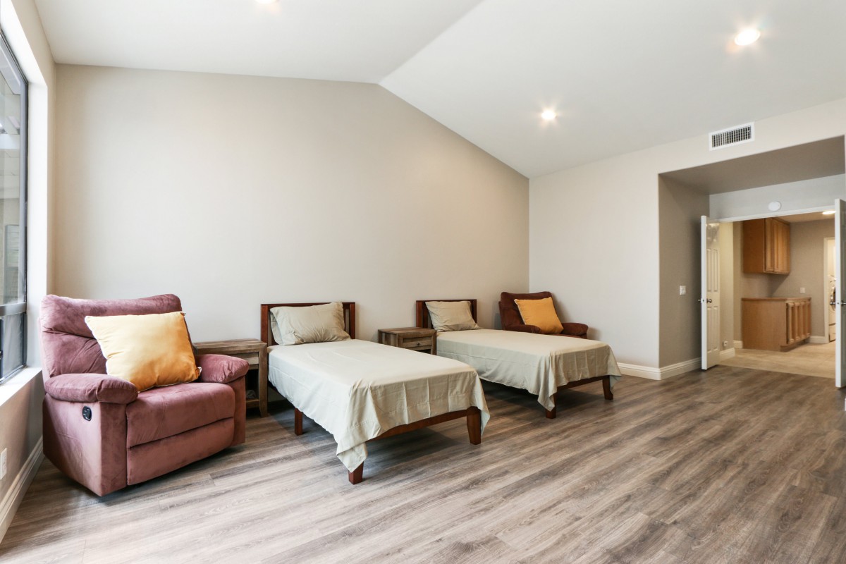 A modern bedroom featuring two twin beds with neutral bedding, a comfortable armchair, and sleek hardwood flooring.