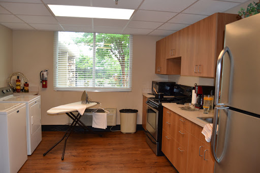 A cozy kitchen space featuring wooden cabinets, appliances, and an ironing board set up by the window.