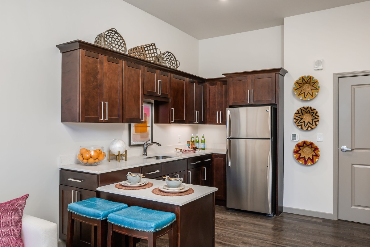 A modern kitchen with dark wood cabinets, stainless steel appliances, and a small breakfast bar with turquoise stools.