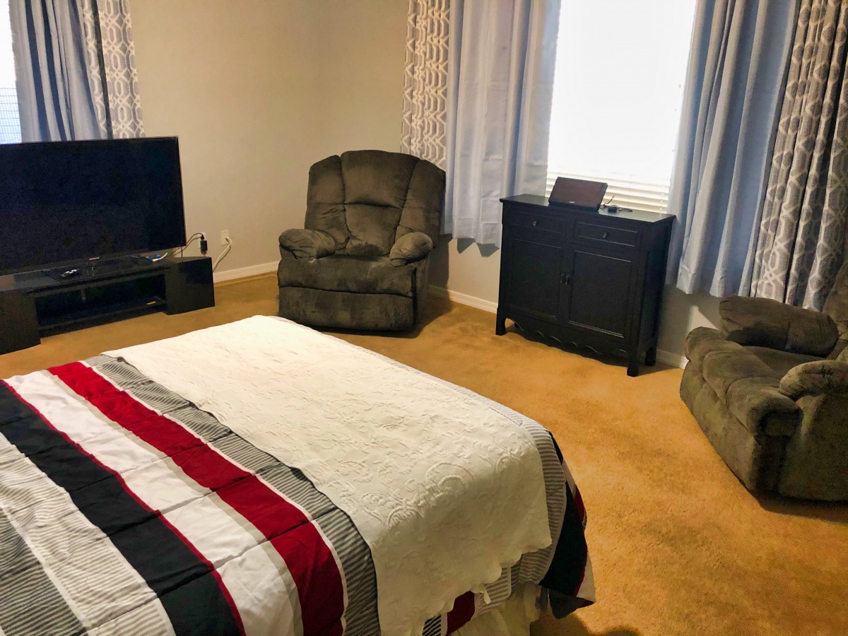 A cozy bedroom with a bed, armchair, dresser, and television.