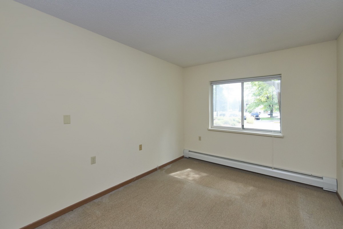 An empty room with carpet flooring and a window letting in natural light.