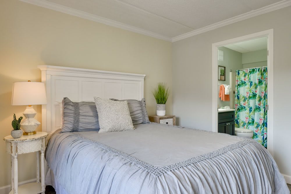 A cozy bedroom with a neatly made bed, pillows, and a nightstand with a potted plant.