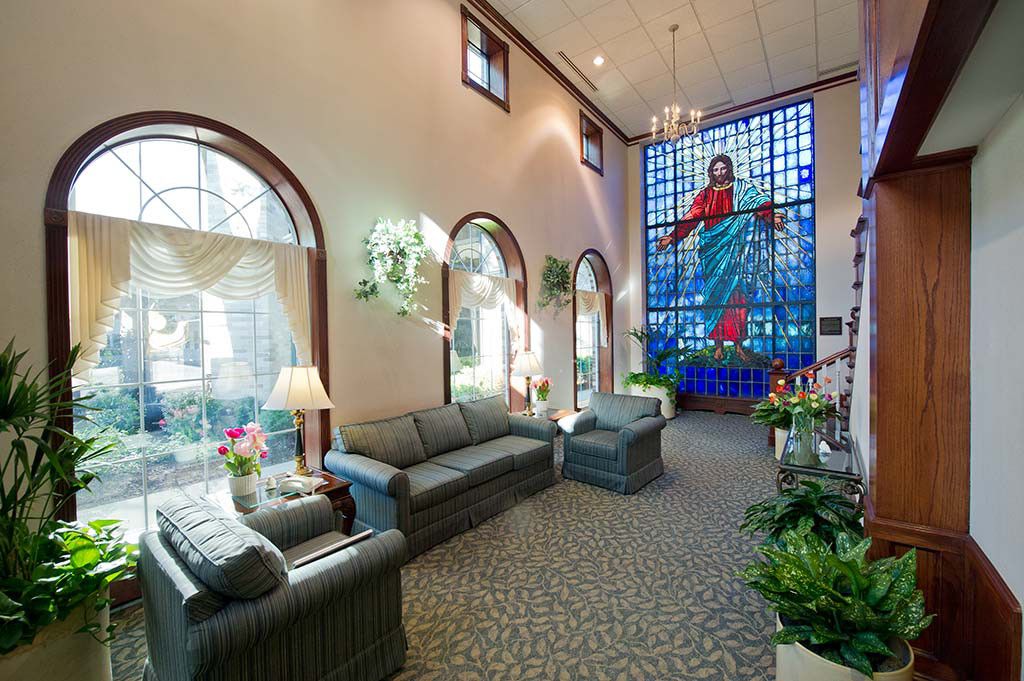 A well-lit lobby with comfortable seating and a prominent stained glass window depicting a religious scene.