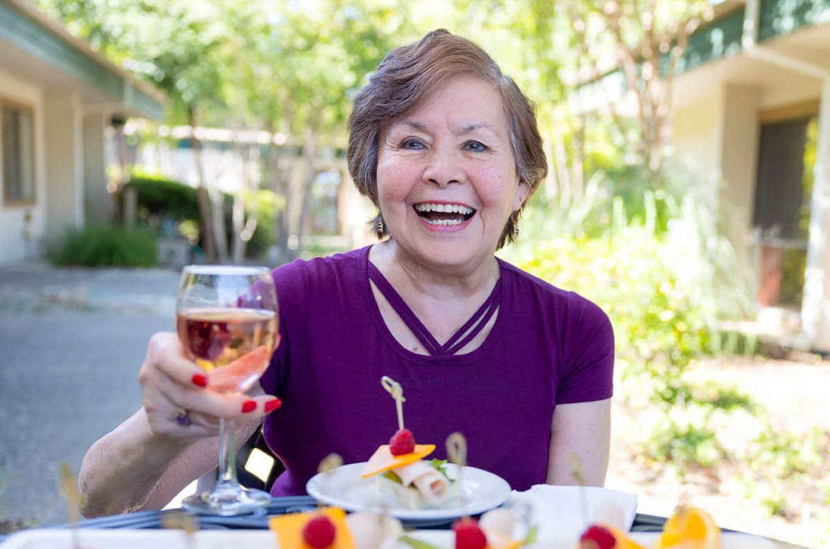 A woman enjoying a meal outdoors with a glass of wine.