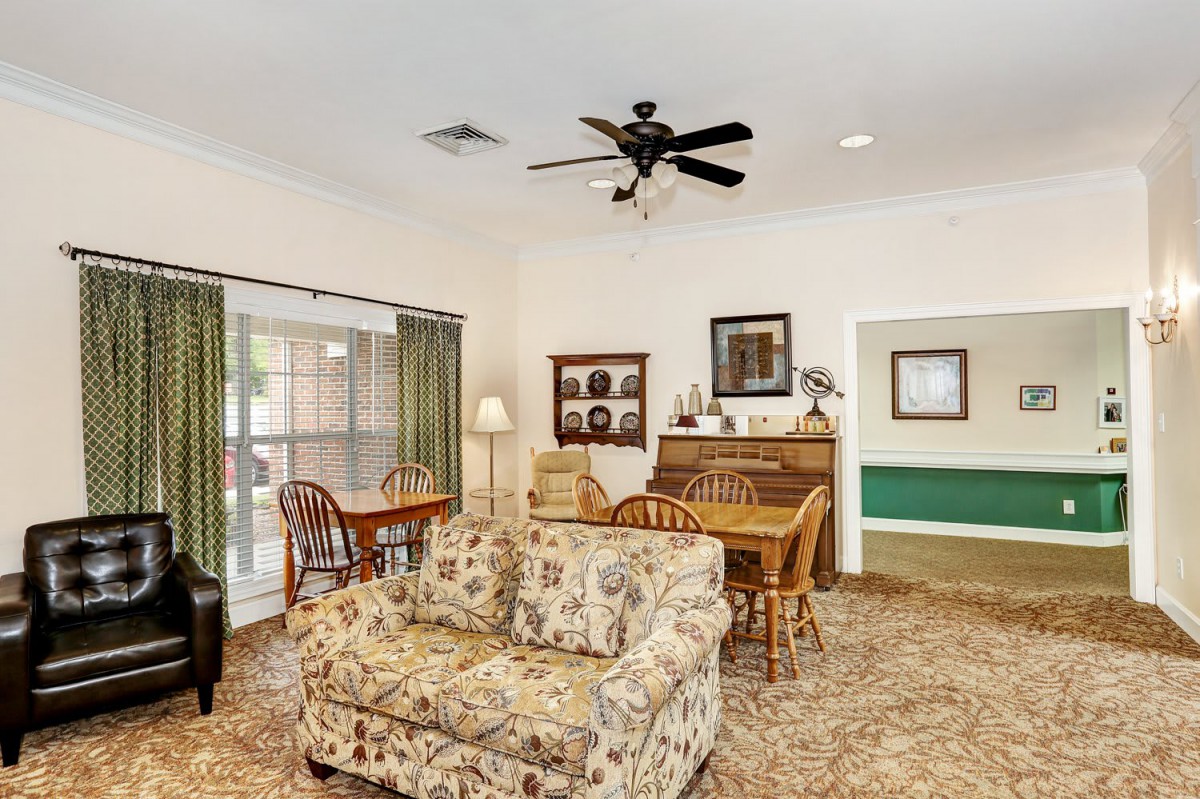 A cozy living room with a floral sofa and dining area, featuring a ceiling fan and decorative elements.