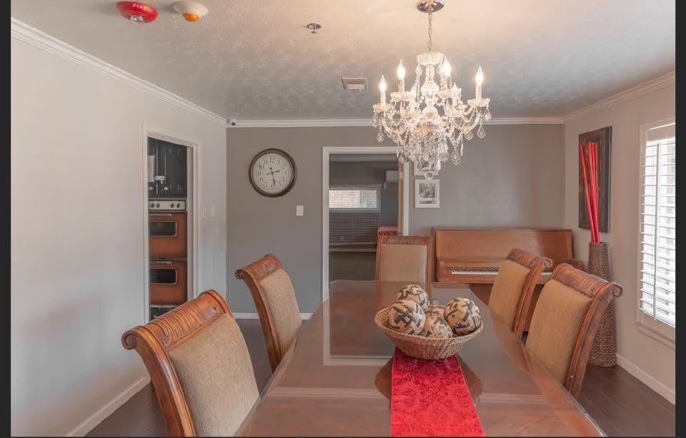 A dining room with a chandelier, table, and chairs, featuring elegant decor and a wall clock.