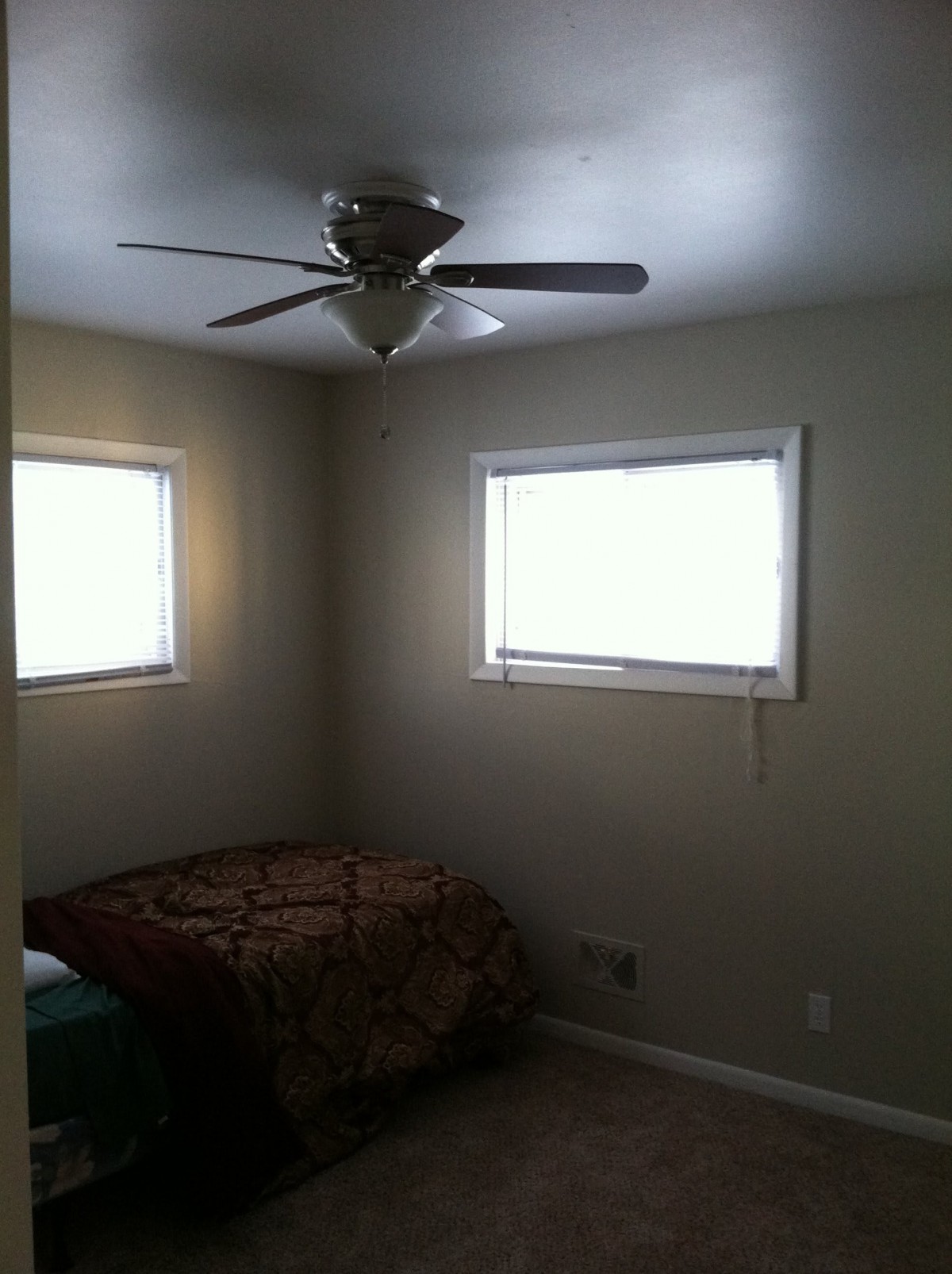 A minimalist bedroom featuring a ceiling fan, two windows, and a simple bed.