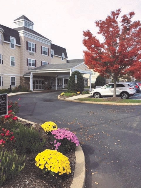 A building entrance surrounded by autumn foliage and colorful flowers.