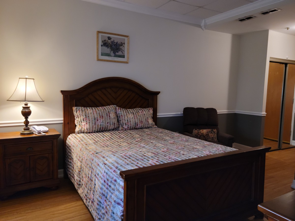 A cozy bedroom featuring a wooden bed with patterned bedding, a nightstand with a lamp, and wall decor.