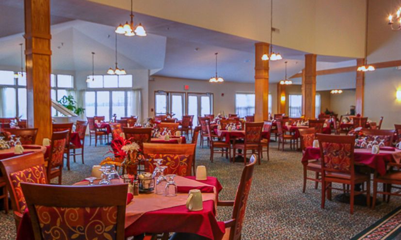An elegant dining room setup with multiple tables and chairs, each adorned with red tablecloths and arranged cutlery.