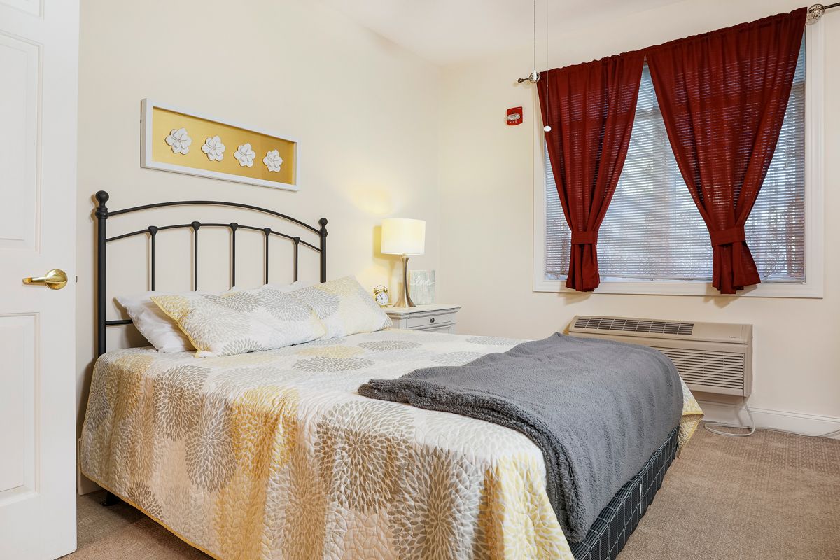 A cozy bedroom with a neatly made bed, bedside lamp, and red curtains.