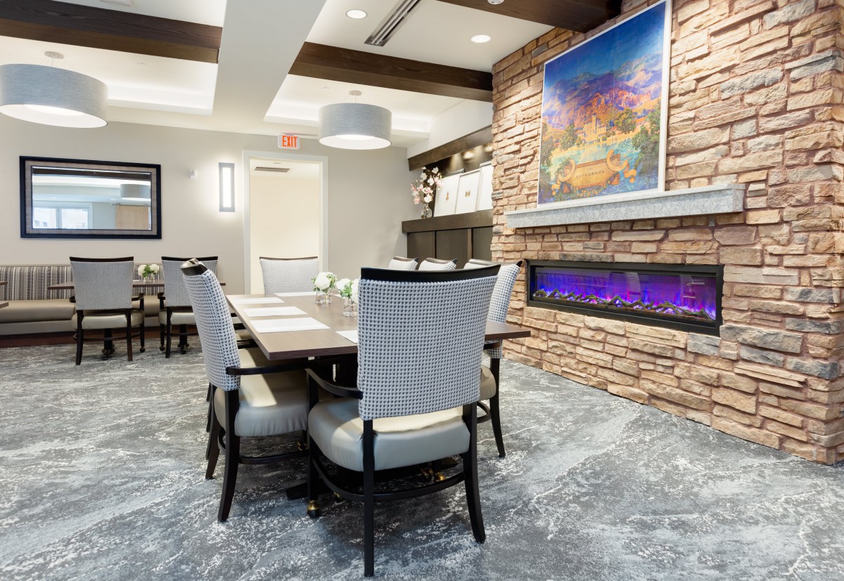 A modern dining room featuring a sleek table and chairs set, with a vibrant piece of artwork above a stone fireplace.