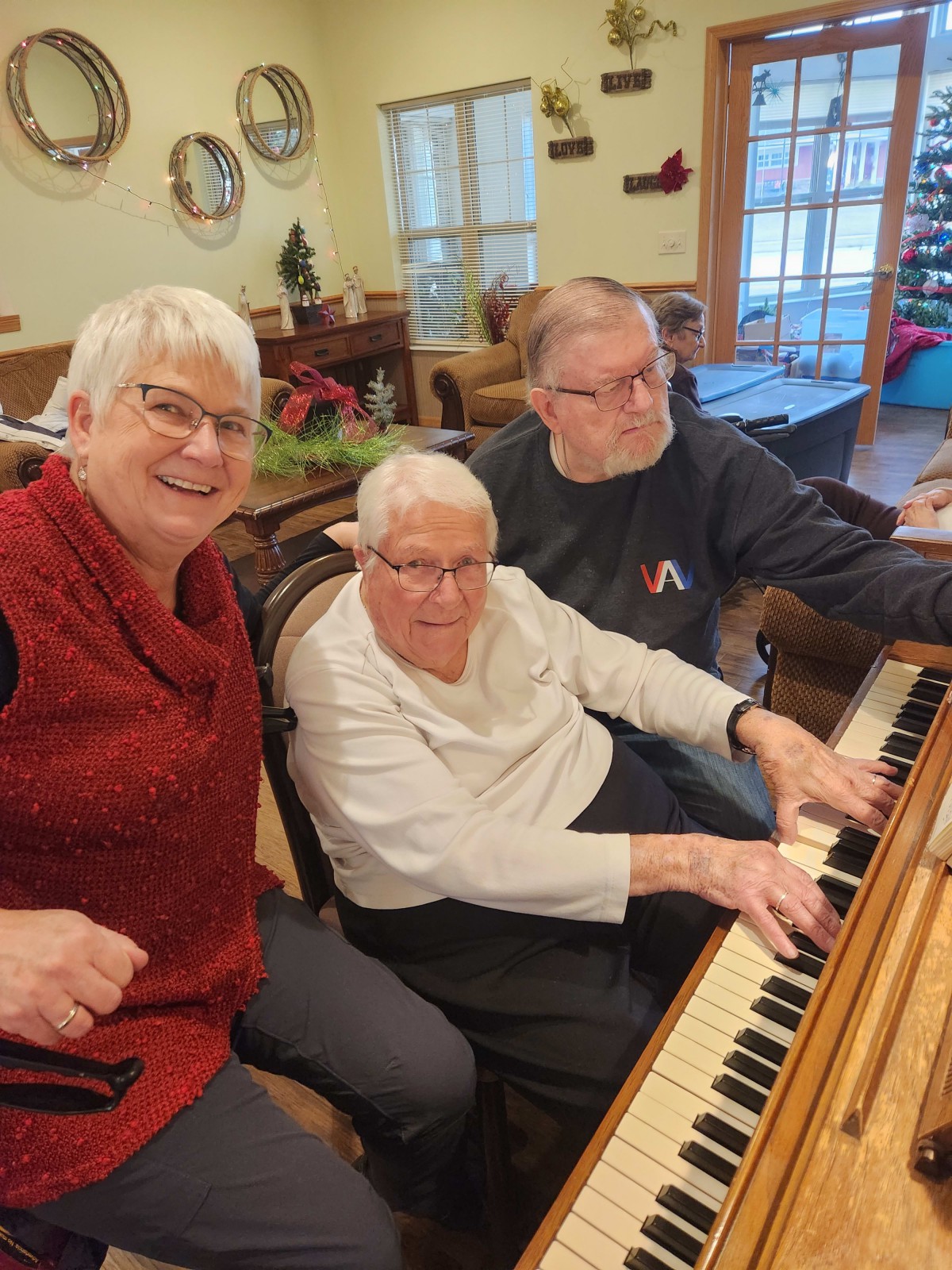 A group of people gathered around a piano, smiling and enjoying each other's company indoors.