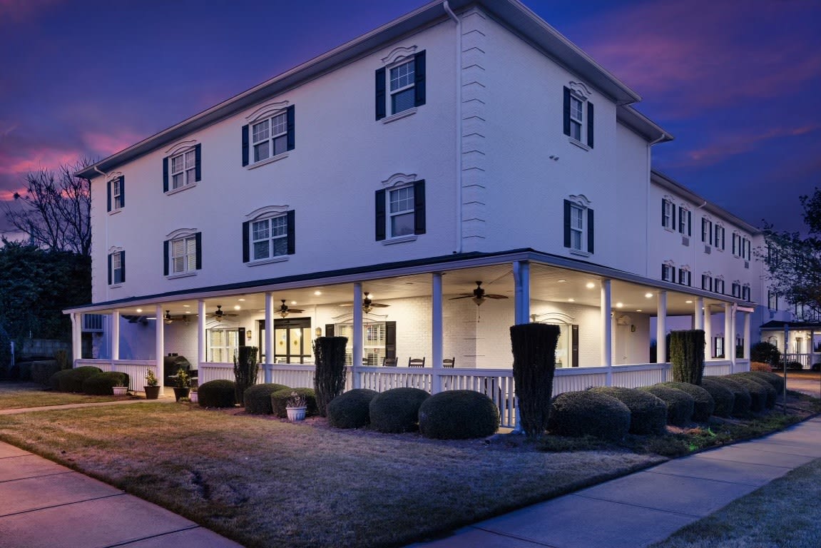 A beautifully lit three-story house with a spacious porch during the evening.