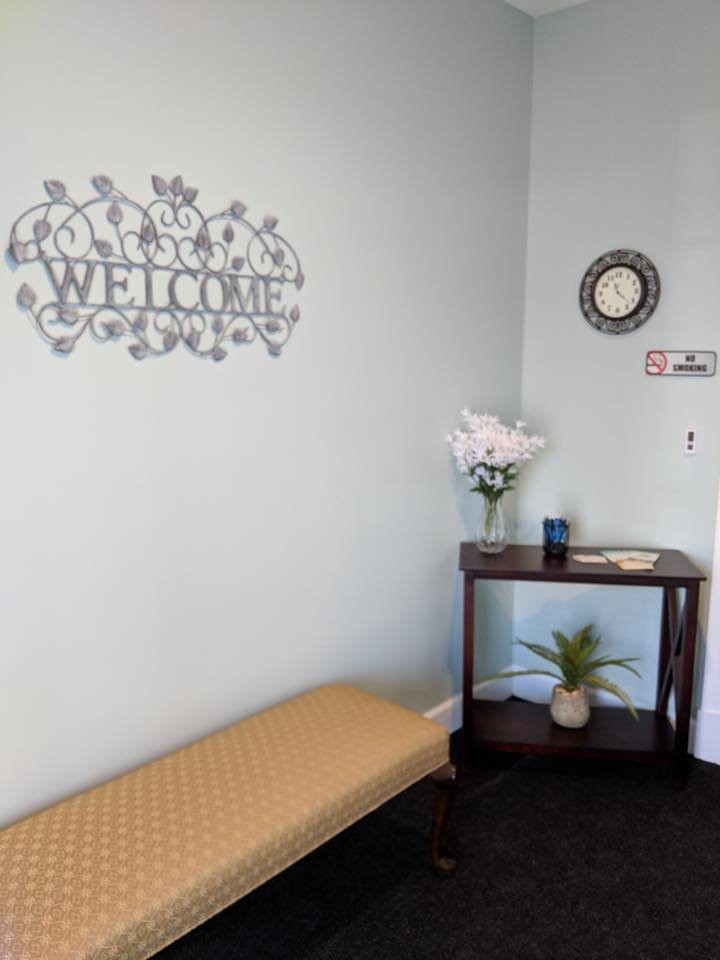A welcoming waiting area with a bench, decorative wall piece, and table with flowers.