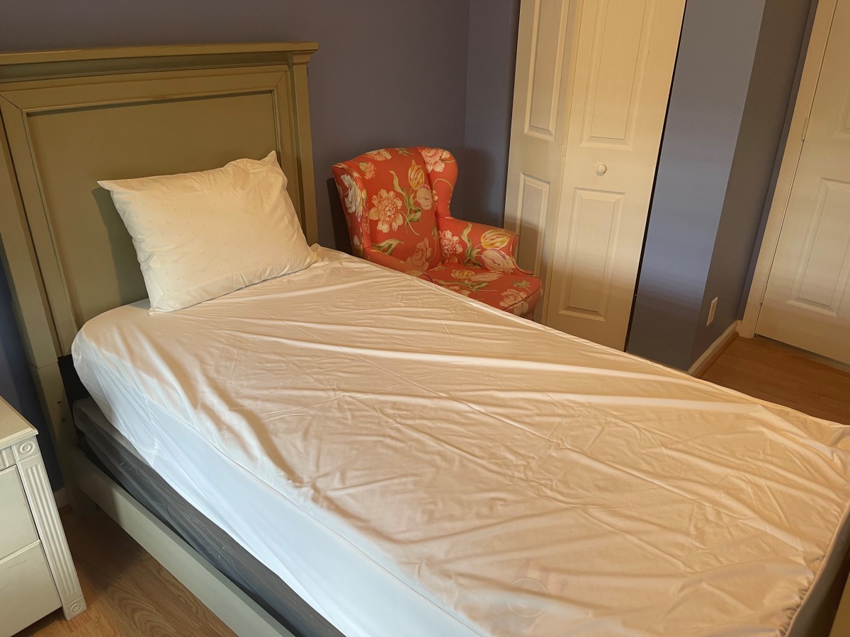 A cozy bedroom featuring a single bed with white bedding and a floral armchair.
