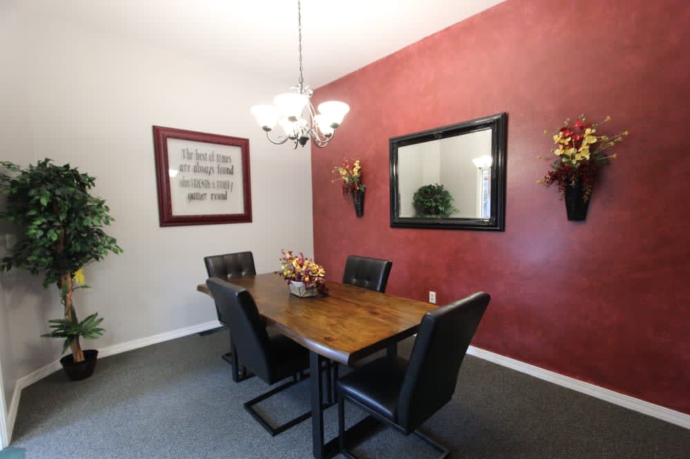 A modern dining room with a wooden table and black chairs, featuring a red accent wall with decorative elements and a mirror.