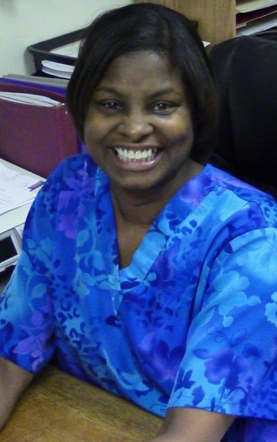 A woman smiling while seated at an office desk wearing blue clothing.