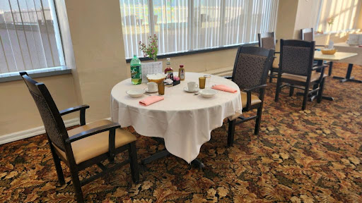 A neatly set dining table with chairs, adorned with a white tablecloth and various items for beverages.