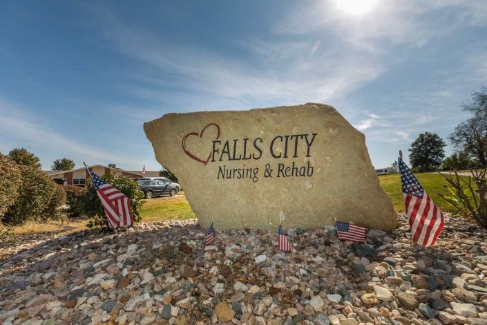 A large stone sign for Falls City Nursing & Rehab set against a clear blue sky.