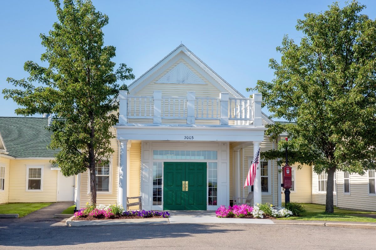 Front view of a building with a green door, flanked by trees and colorful flowers.