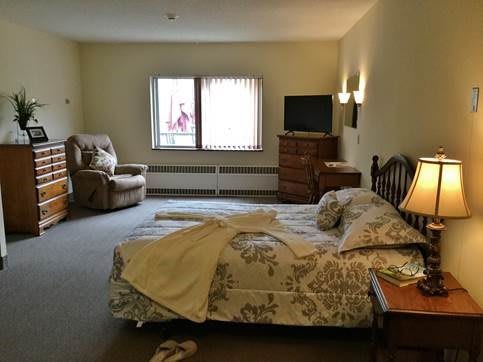A cozy bedroom with a bed, chair, dresser, and television.