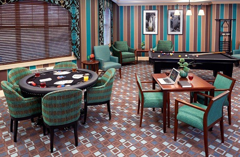 A stylish gaming room featuring a poker table, comfortable chairs, and a green and brown color theme with striped wallpaper.