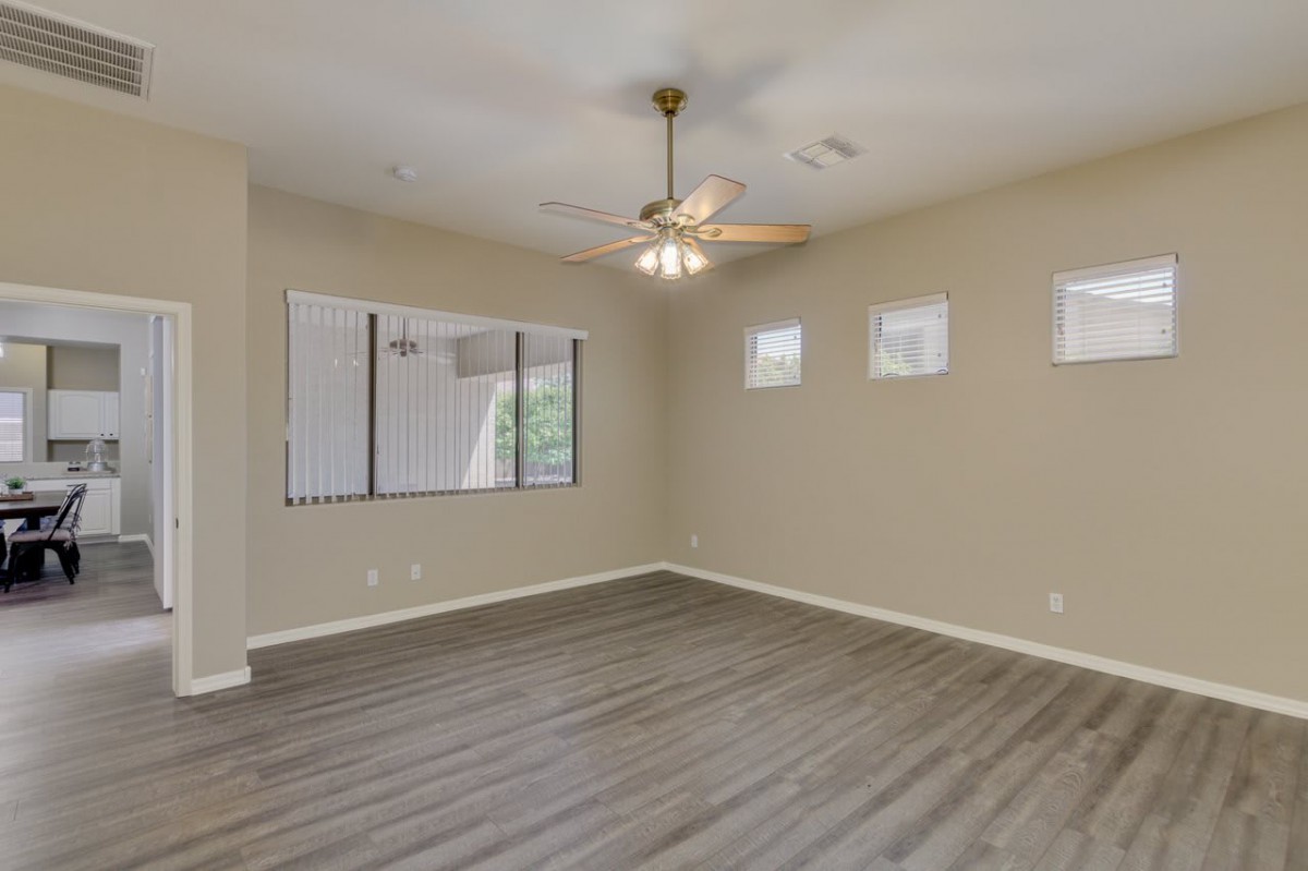 An empty room with wood flooring, a ceiling fan, and several windows allowing natural light.