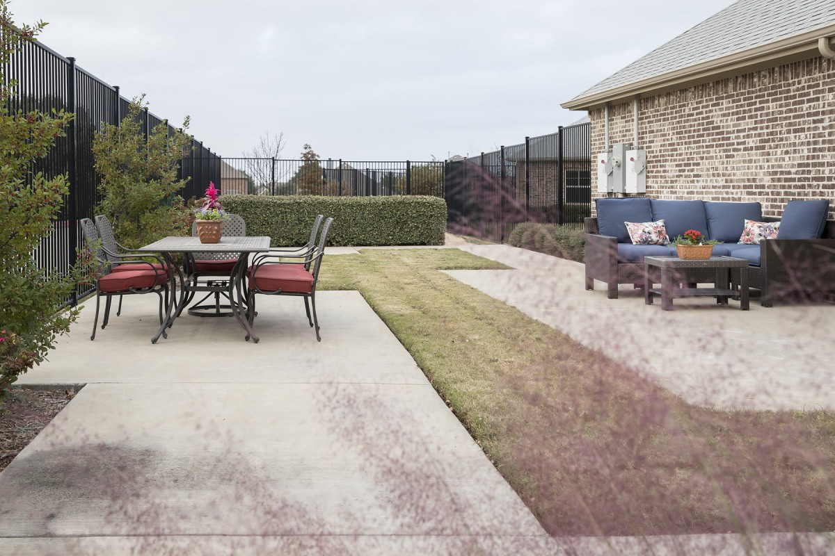 A spacious backyard patio with outdoor furniture and a well-maintained lawn beside a stone house.
