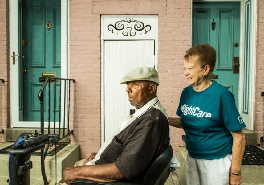 A caregiver assisting an elderly man in a wheelchair outside a building.