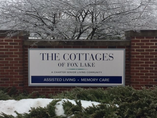 A sign for The Cottages of Fox Lake, advertising assisted living and memory care services, with a snowy background.