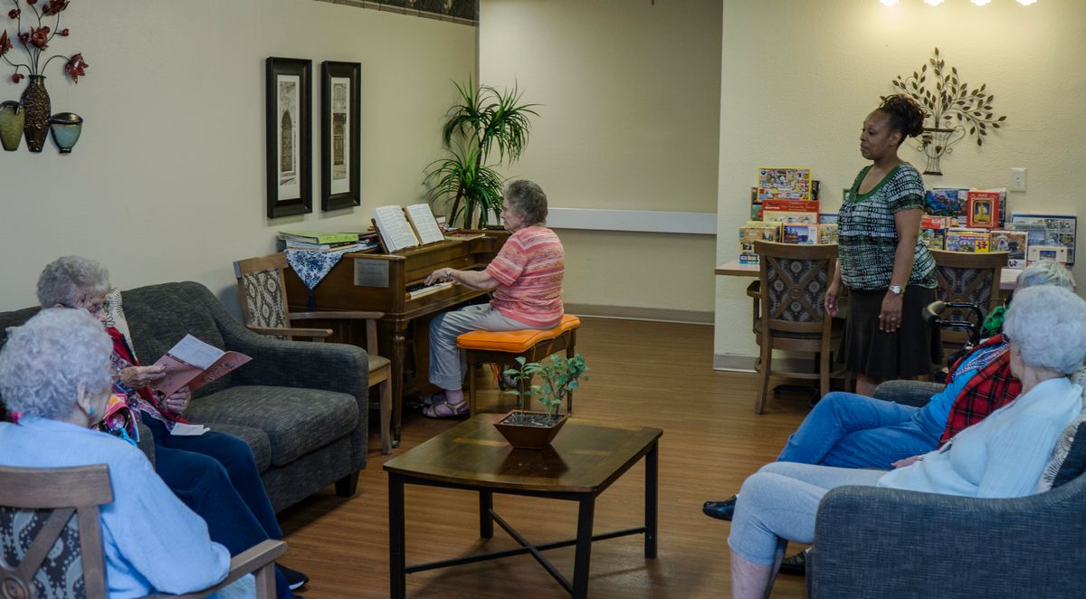 An elderly woman plays the piano in a cozy living room setting.
